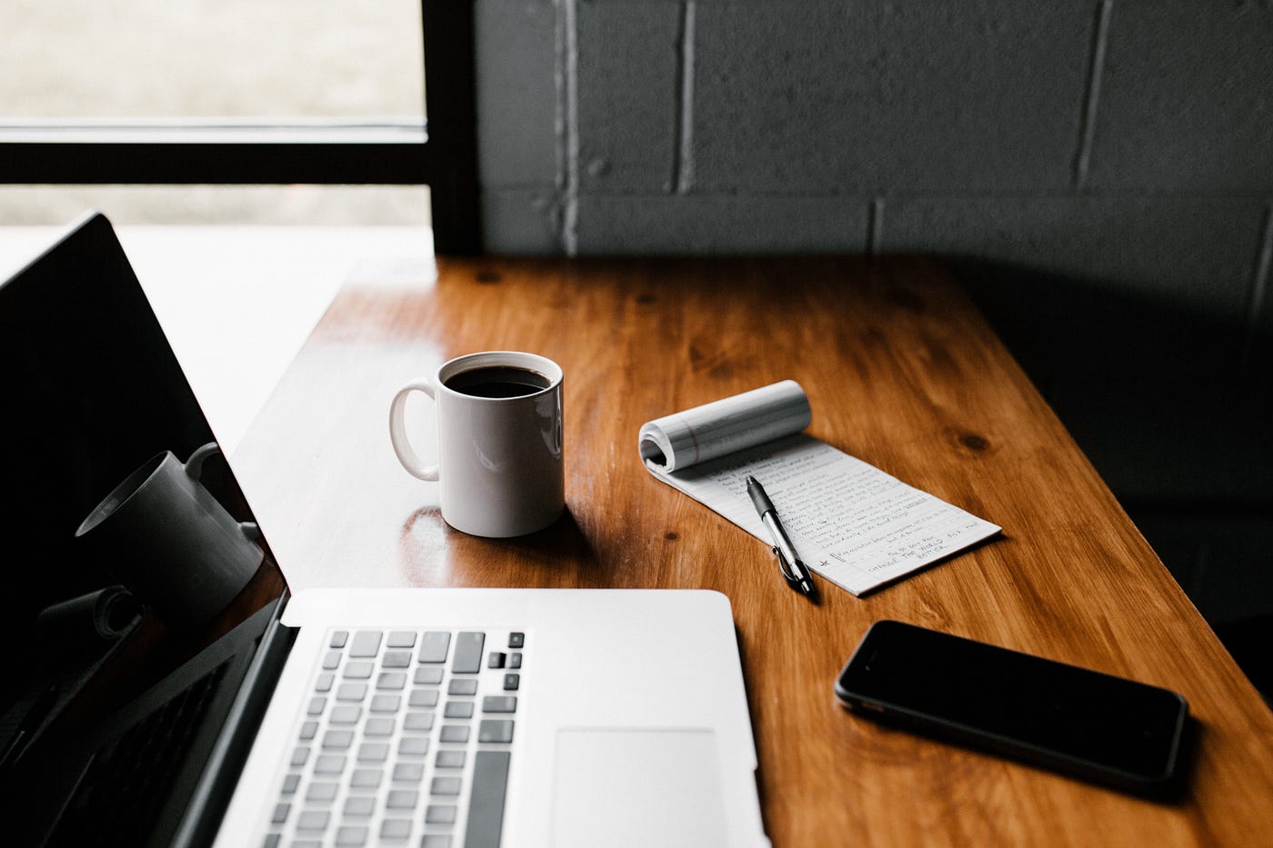 photo of laptop, coffee mug, phone and notepad on desk