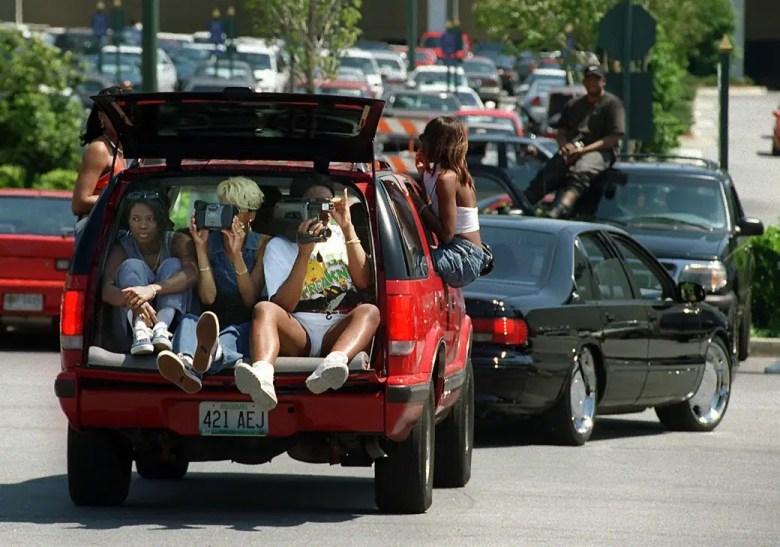 a group of young Black college-age women sit in the back of a red minivan