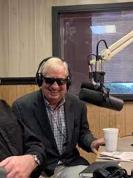 Delk Kennedy in sunglasses sits before a radio mic (Facebook)