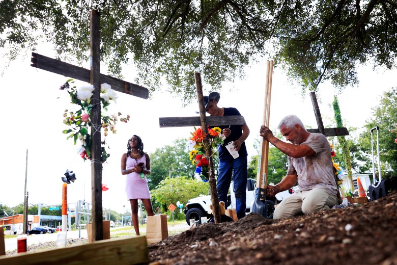 From left, a woman who goes by the name of "Queen," views crosses put up in memory of the victims of Saturday's shooting as artist Roberto Marquez, of Dallas, paints and Will Walsh, of Nocatee, Fla., helps construct posts Monday, Aug. 28, 2023, near the site of the attack at a Dollar General store in Jacksonville, Fla. Queen says she is a manager at the store and was holed up in the office at the store when the shooting occurred. 