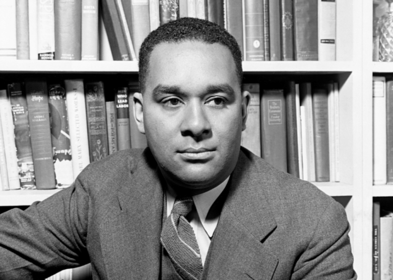 Portrait of novelist Richard Wright seated in front of bookshelf.