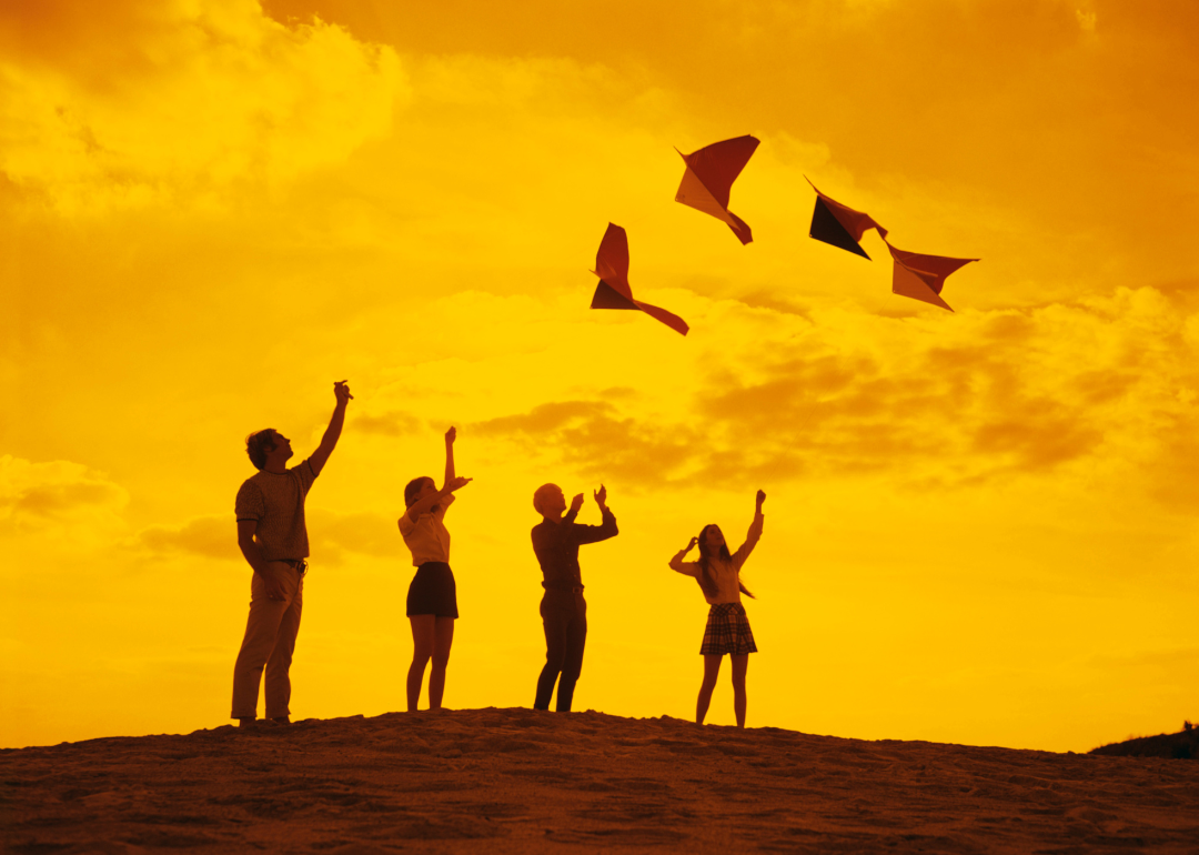 Friends flying kites on a hill at sunset.