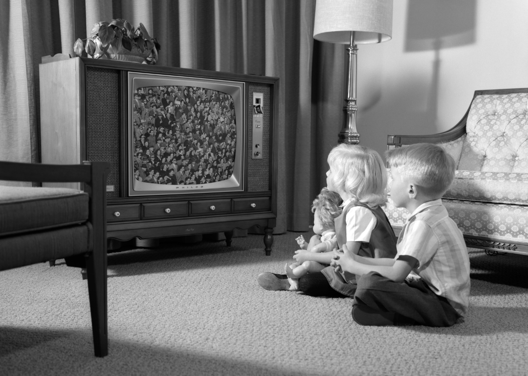 Two siblings sitting on the floor watching tv.